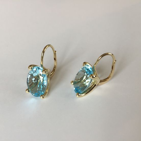 Ein Paar goldplattierter Ohrringe mit blauen Topas-Edelsteinen, auf einem weißen Hintergrund platziert.