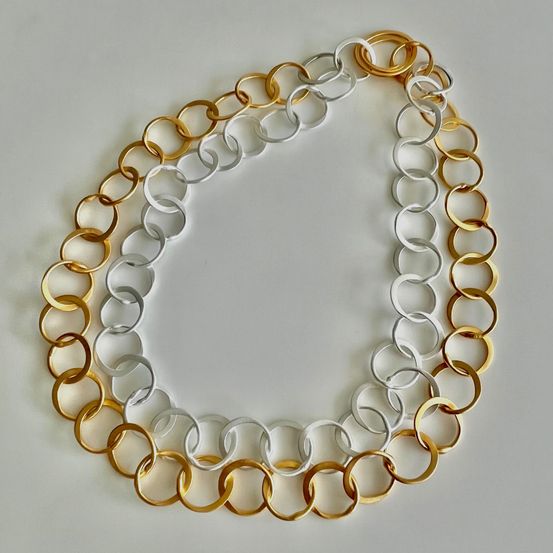 Eine Gold- und Silberkette mit abwechselnd großen und kleinen Ringen auf einer weißen Oberfläche.