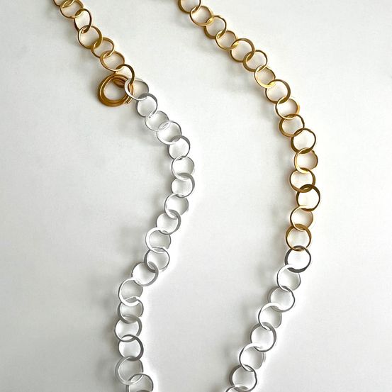 Eine Halskette aus Gold- und Silberglieder mit runden Ringen wird auf weißem Hintergrund gezeigt. Die Kette hat abwechselnd goldene und silberne Ringe.