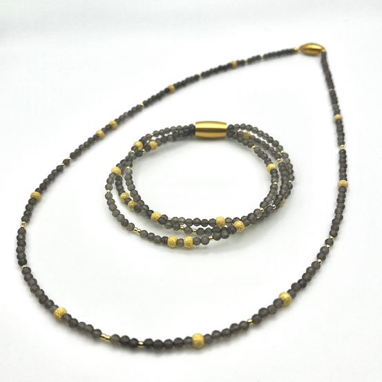 Ein Schmuckset mit einer schwarzen Perlenkette mit goldenen Akzenten und einem passenden Armband, präsentiert auf weißem Hintergrund.