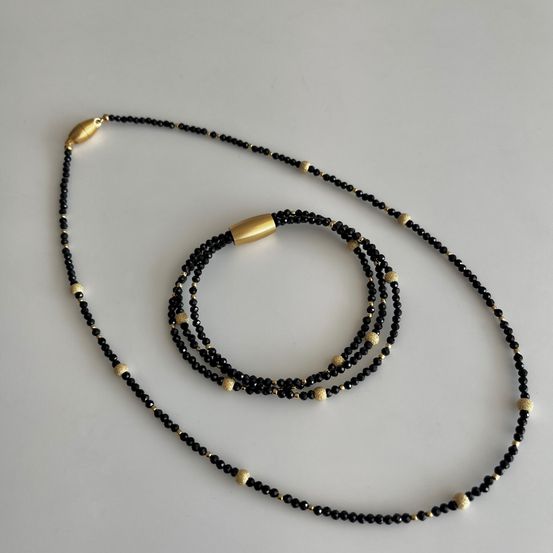Ein Set mit drei schwarzen und goldenen Perlenketten auf einer weißen Oberfläche.