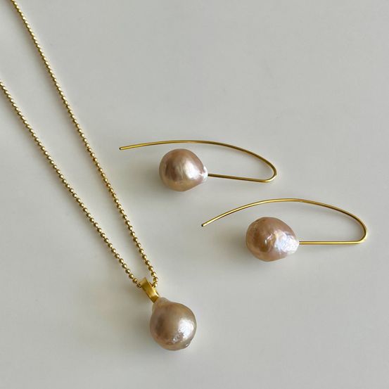 Ein Set aus vergoldetem Schmuck mit rosa Perlen. Das Set besteht aus einer Halskette und zwei Ohrringen. Die Perlen sind groß und glänzend.