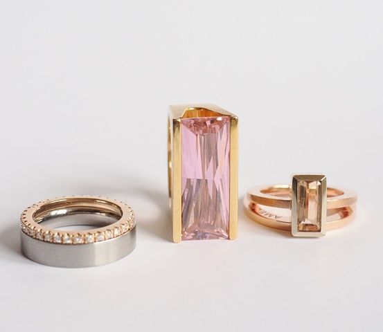 Drei Ringe sind auf einem weißen Hintergrund zu sehen: ein Goldring, ein Roségoldring und ein Silberring. Der mittlere Ring ist größer mit einem rosa Edelstein.