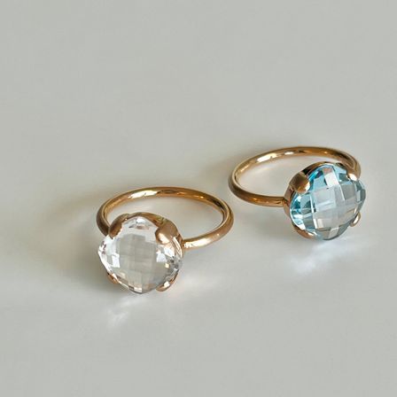 Zwei goldene Ringe mit großen klaren und blauen Topas-Edelsteinen werden auf einer weißen Oberfläche gezeigt.