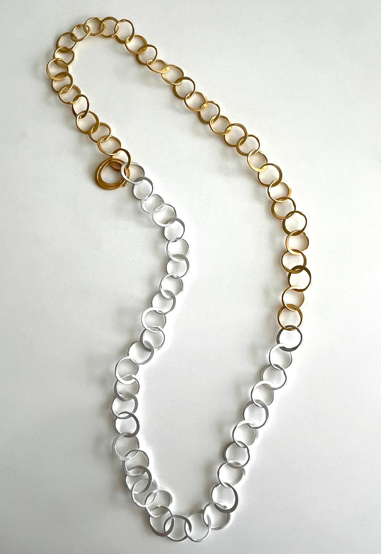 Eine lange Halskette mit abwechselnden goldenen und silbernen kreisförmigen Gliedern auf weißem Hintergrund.