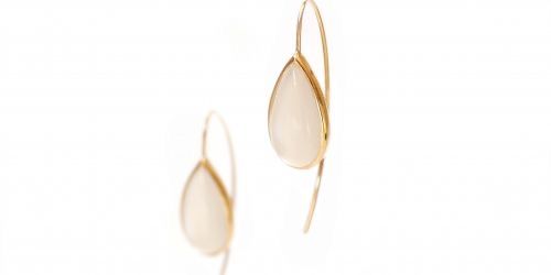 Zwei goldplattierte Ohrringe mit tropfenförmigen weißen Steinen hängen vor einem weißen Hintergrund.