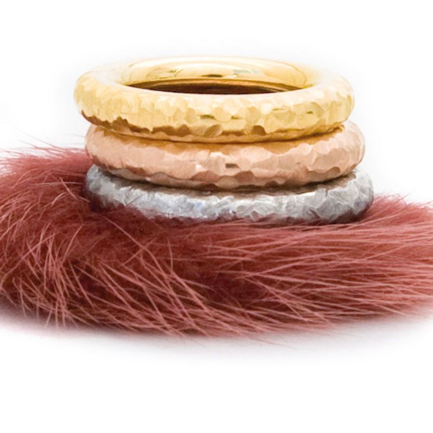 Drei metallische Ringe, Gold, Roségold und Silber, gestapelt auf einem rosa Pelzstoff.