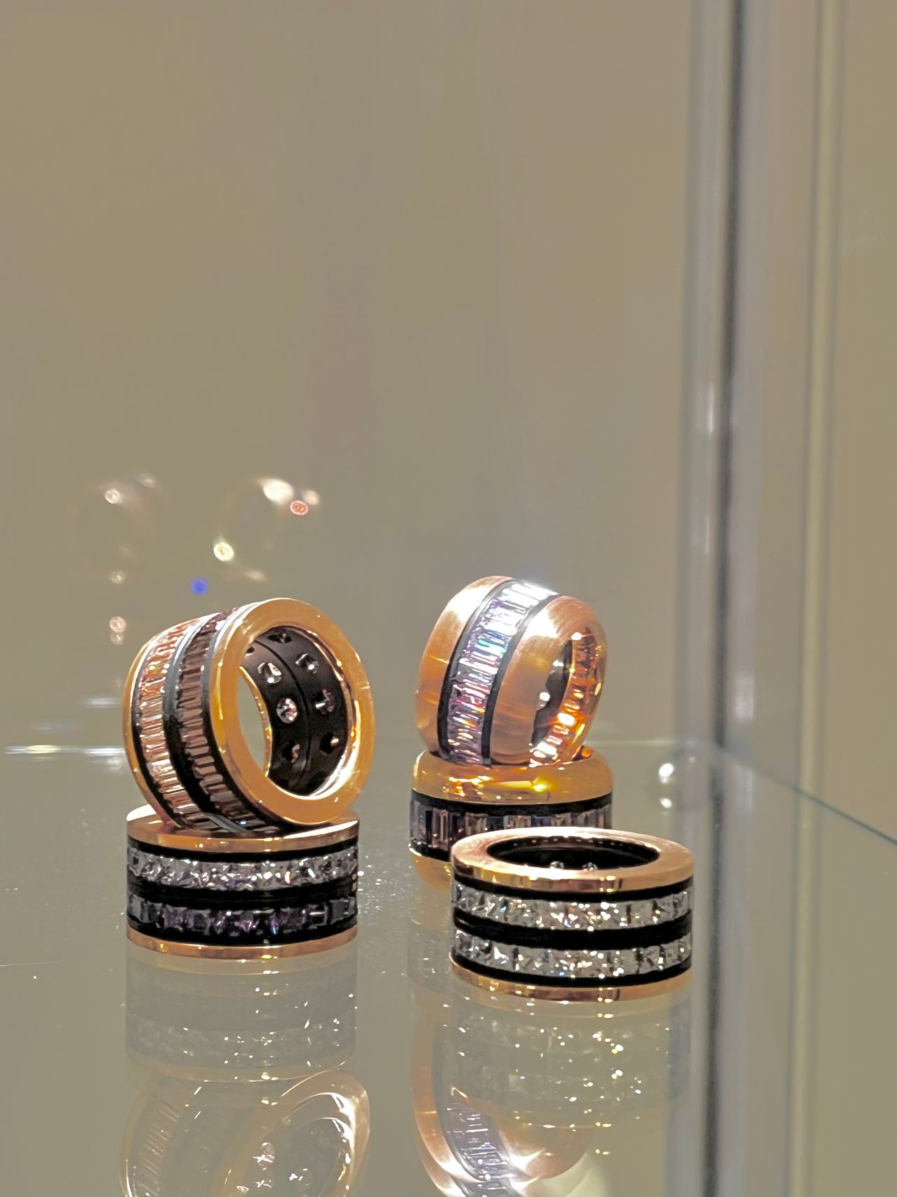 Drei goldene Ringe mit schwarzen und weißen Edelsteinen auf einer Glasfläche, die Licht reflektieren.