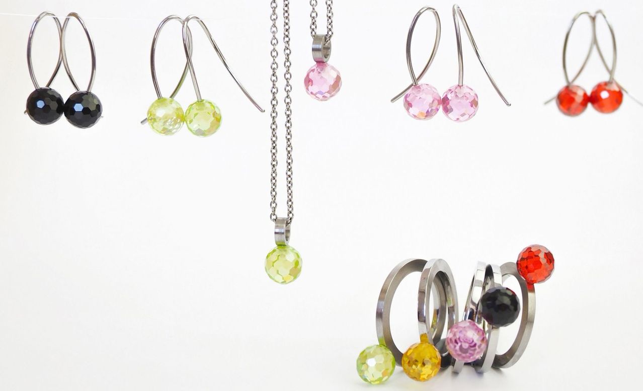 Verschiedene Schmuckstücke mit farbigen Kristallperlen, einschließlich Ohrringe, Halsketten und Ringe, auf weißem Hintergrund präsentiert.