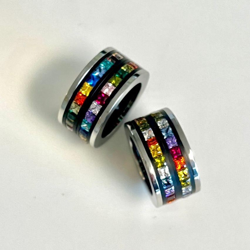 Zwei Edelstahlringe mit bunten Kristallen auf einer weißen Oberfläche. Die Ringe sind mit bunten Edelsteinen gestapelt.