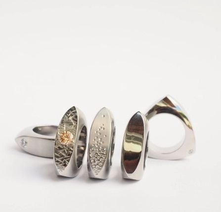 Fünf Silberringe mit einzigartigen Designs sind in einer Reihe angeordnet. Jeder Ring weist komplizierte Texturen und Muster auf. Der zweite Ring von links hat einen gelben Edelstein in der Mitte.