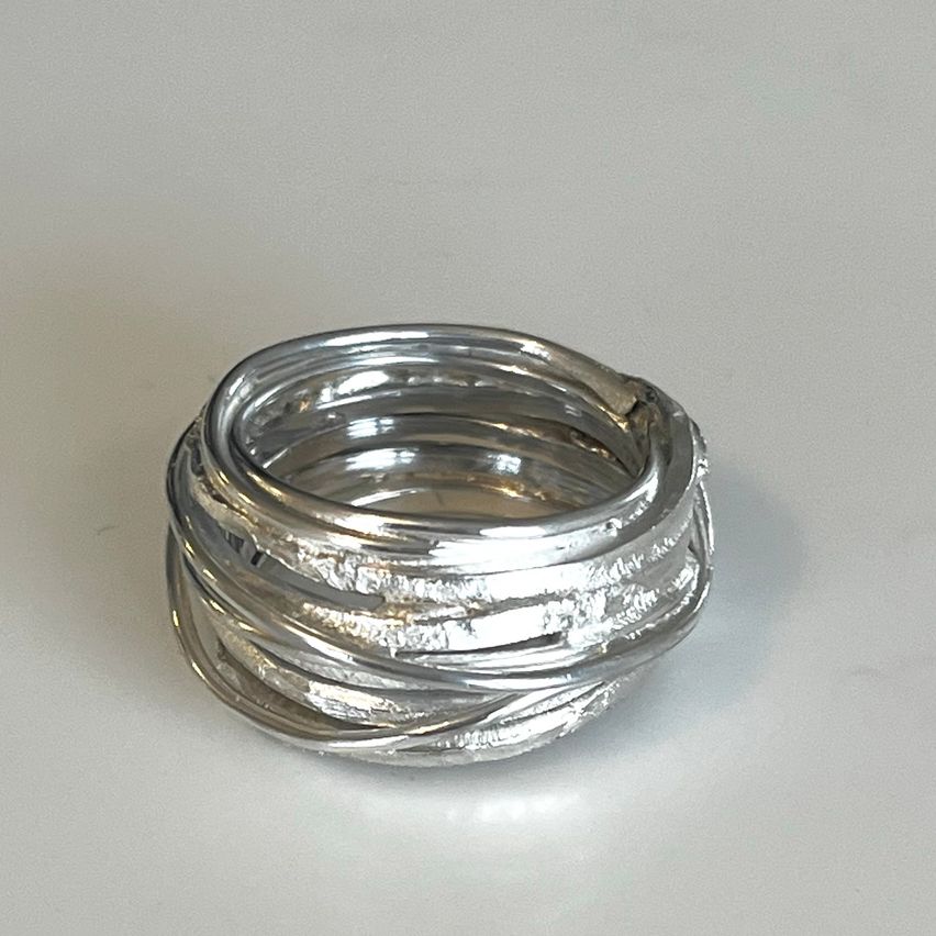 Ein Stapel silberner Ringe mit verzwirbeltem Design, auf einer hellen Oberfläche liegend. Die Ringe haben eine glänzende, metallische Oberfläche.