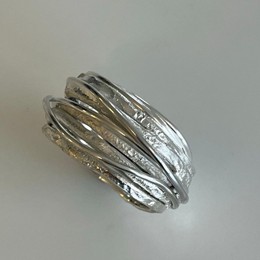 Ein Nahaufnahme eines silbernen Rings mit strukturierten, welligen Mustern auf hellem Hintergrund.