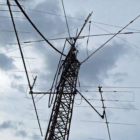 Ein hoher Metall-Kommunikationsturm mit zahlreichen Antennen und Kabeln unter einem bewölkten Himmel.