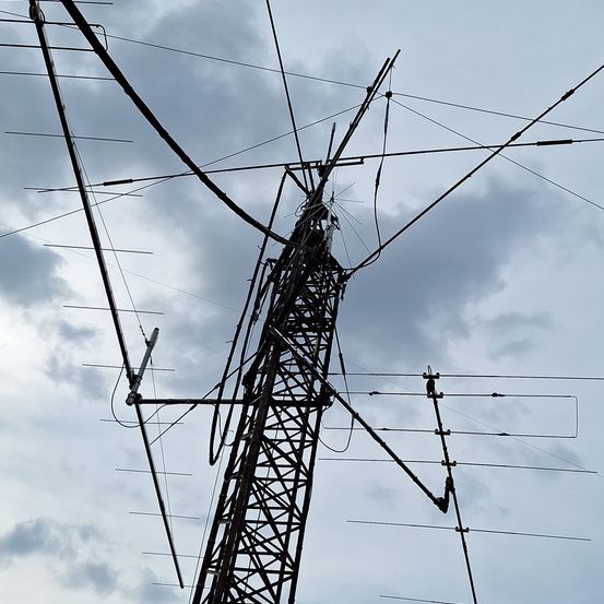 Ein hoher Metall-Kommunikationsturm mit zahlreichen Antennen und Kabeln unter einem bewölkten Himmel.