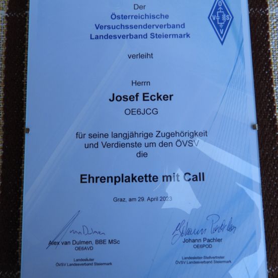 Eine Auszeichnungsplakette, die von der Österreichischen Amateurfunkvereinigung Landesverband Steiermark verliehen wurde, überreicht an Herrn Josef Ecker für langjährige Mitgliedschaft und Verdienste um den OeVSV. Datum: 29. April 2023, unterzeichnet von Alex van Dulmen und Johann Pachler.