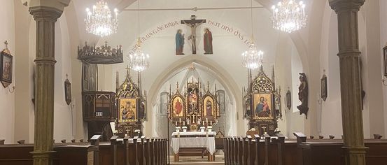 Der Innenraum einer Kathedrale mit hölzernen Kirchenbänken, einem Altar und einem Kruzifix, geschmückt mit Kronleuchtern und religiösen Kunstwerken.