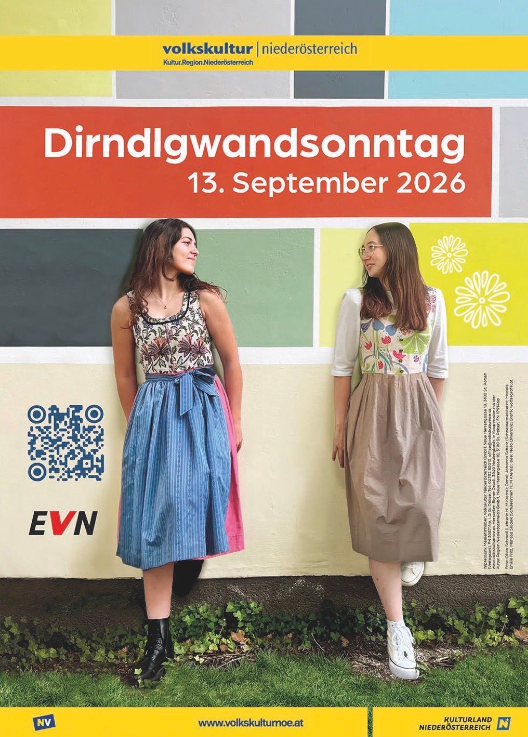 Zwei Frauen in traditioneller Kleidung stehen vor einer bunten Wand mit dem Text 'Dirndlgwandsonntag 13. September 2026'. Die Frau links trägt ein blaues Kleid, die Frau rechts ein braunes Kleid.