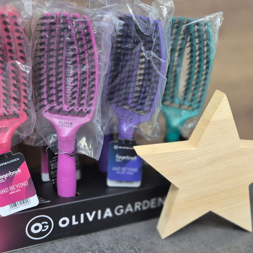 Vier Olivia Garden Haarbürsten sind in Plastik verpackt, einschließlich rosa, lila und türkisfarbener Bürsten. Ein Holzstern steht neben der Schachtel.