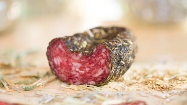 Eine Nahaufnahme eines geschnittenen Stücks Wurst, teilweise geschnitten und mit Kräutern bestreut, auf einem Holzbrett.