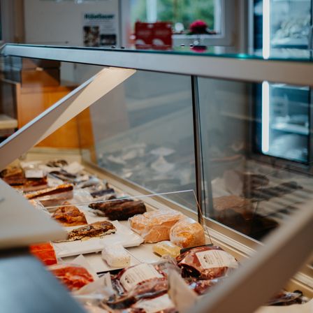 Ein gekühlter Tresen mit einer Glasvitrine ist mit verschiedenen Lebensmitteln gefüllt, darunter Brot, Gebäck und Fleisch. Der Tresen ist gut beleuchtet und die Vitrine ist transparent.