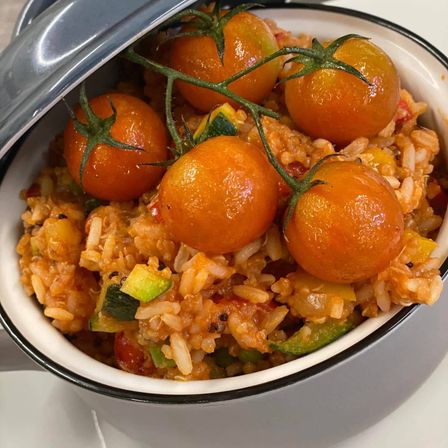Ein Teller mit Reis, Zucchini, Tomaten und anderen Gemüsen, gekrönt von Kirschtomaten, liegt auf einem weißen Teller.