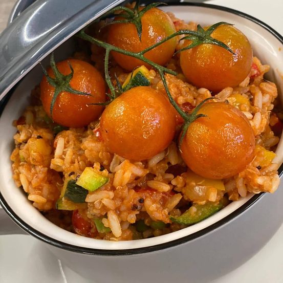 Ein Teller mit Reis, Zucchini, Tomaten und anderen Gemüsen, gekrönt von Kirschtomaten, liegt auf einem weißen Teller.