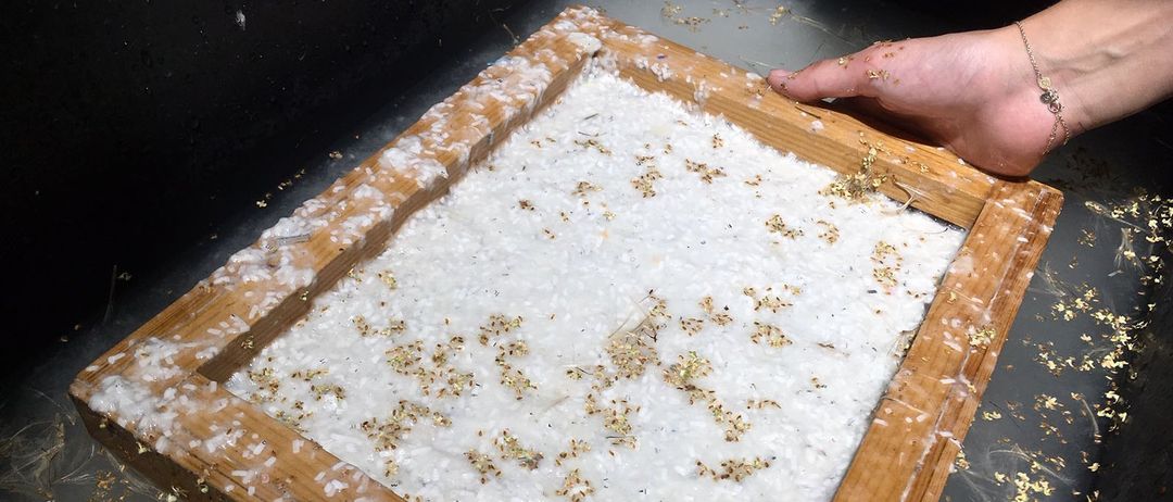 Ein hölzerner Rahmen, gefüllt mit weißem Pulver, möglicherweise eine Art Salz, wird von zwei Händen über einem Wasserbad gehalten. Das Pulver hat winzige goldene und weiße Partikel darauf gestreut.