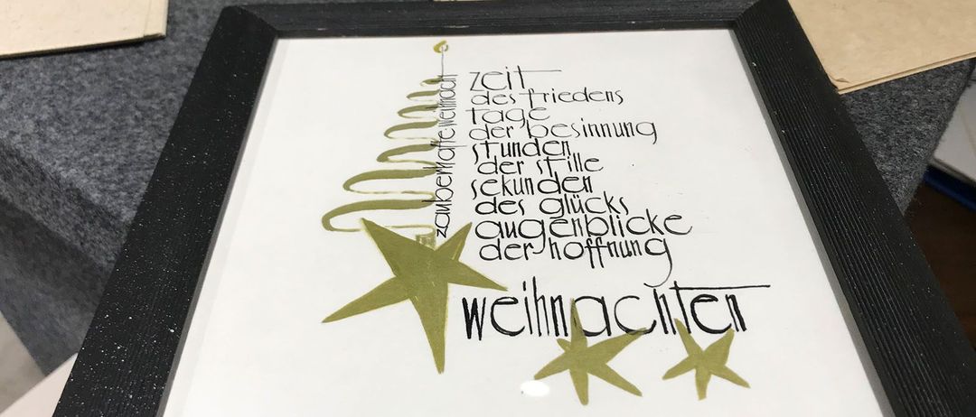 Ein gerahmtes Kunstwerk auf einem Tisch mit einem Weihnachtsbaum-Design und Text auf Deutsch. Papierstreifen sind in der Nähe.