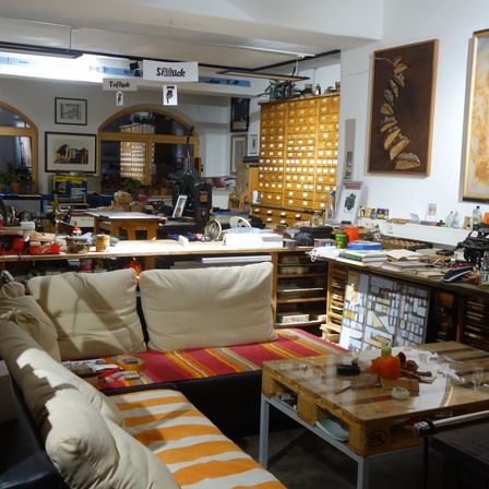 Ein geräumiger Raum mit Holzschränken, Schreibtischen und Sofas. Auf den Tischen befinden sich verschiedene Gegenstände, darunter eine Kürbis. Ein Schild mit der Aufschrift 'Stillhcke' an der Wand.