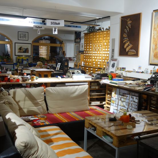 Ein geräumiger Raum mit Holzschränken, Schreibtischen und Sofas. Auf den Tischen befinden sich verschiedene Gegenstände, darunter eine Kürbis. Ein Schild mit der Aufschrift 'Stillhcke' an der Wand.