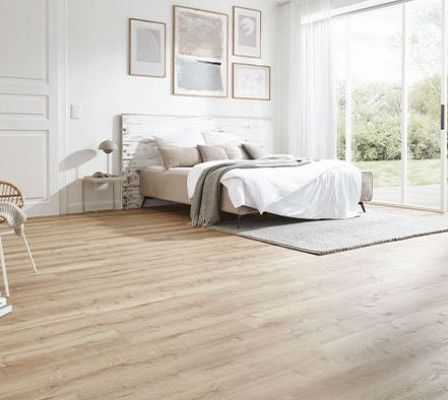 Ein Schlafzimmer mit weißen Wänden, Holzboden und Schiebetüren. Ein Bett mit weißen Laken und Kissen steht in der Nähe der Glastüren.
