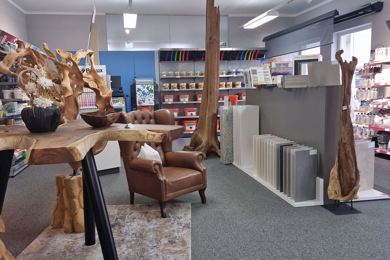 Der Innenraum eines Geschäfts mit einem Holztisch, einem braunen Ledersessel, einem Baumstamm und Regalen mit verschiedenen Produkten.