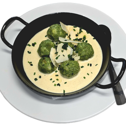 Ein schwarzer Bowl mit grünen Knödeln in einer cremigen Sauce, mit Käse und Petersilie bestreut, auf einem weißen Teller.