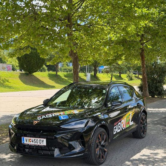 Ein schwarzer SUV mit dem Kennzeichen VI 450 DY ist an einem sonnigen Tag unter Bäumen geparkt. Der vordere Stoßfänger hat eine Rennnummer und den Namen Gabriel in leuchtenden Farben.