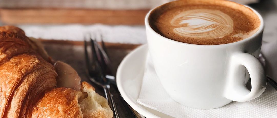 Ein Plakat für ein englisches Sprachcafé in einem Restaurant mit Kaffee, Croissant und Besteck. Das Event findet am 18. April von 10-11 Uhr statt.