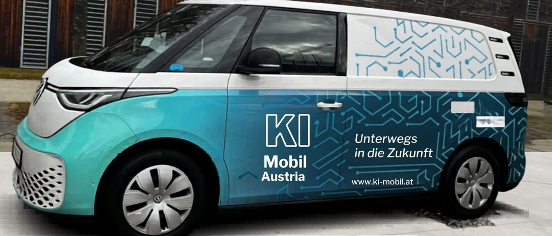 Blauer und weißer Elektrowagen mit KI Mobil Austria Logo auf einer Straße geparkt. Der Wagen hat blaue Schaltkreisdesigns und eine Website auf der Seite.