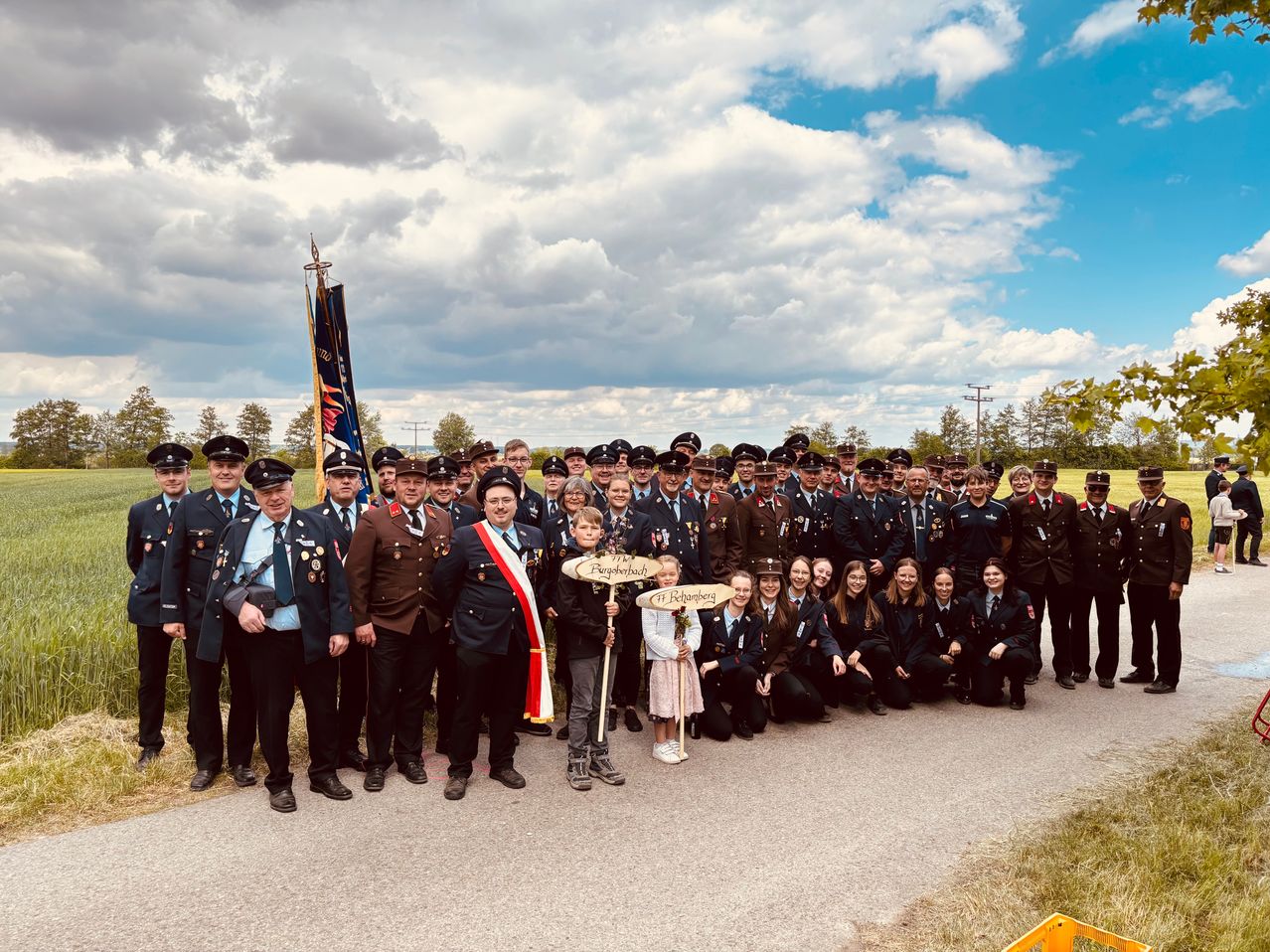 Eine Gruppe uniformierter Personen, darunter Männer, Frauen und Kinder, stehen auf einer Straße und posieren für ein Foto bei bewölktem Himmel.