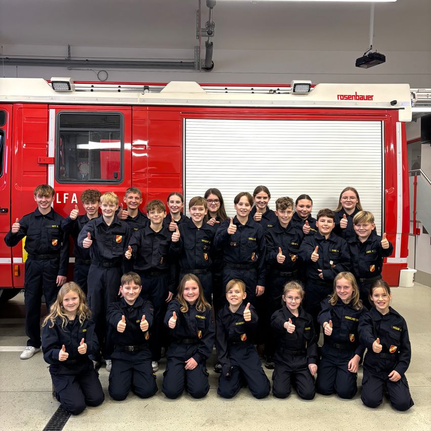 Eine Gruppe junger Personen in Uniformen posiert für ein Foto vor einem Feuerwehrauto.