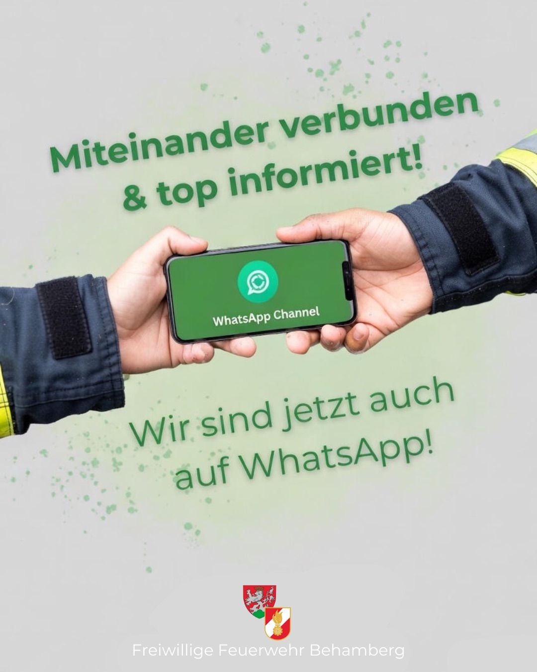 Zwei Hände halten ein Smartphone mit offenem WhatsApp-Kanal, grüner Hintergrund mit weißem Text, eine Hand in einem blauen Jackett und die andere in einem blauen Jackett mit gelbem Streifen.
