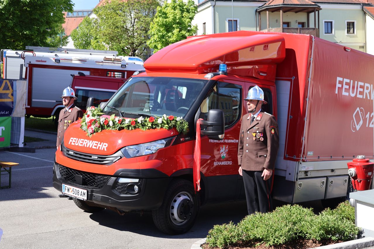 A fire truck with flowers on the front is parked on the street. A firefighter is standing beside it.