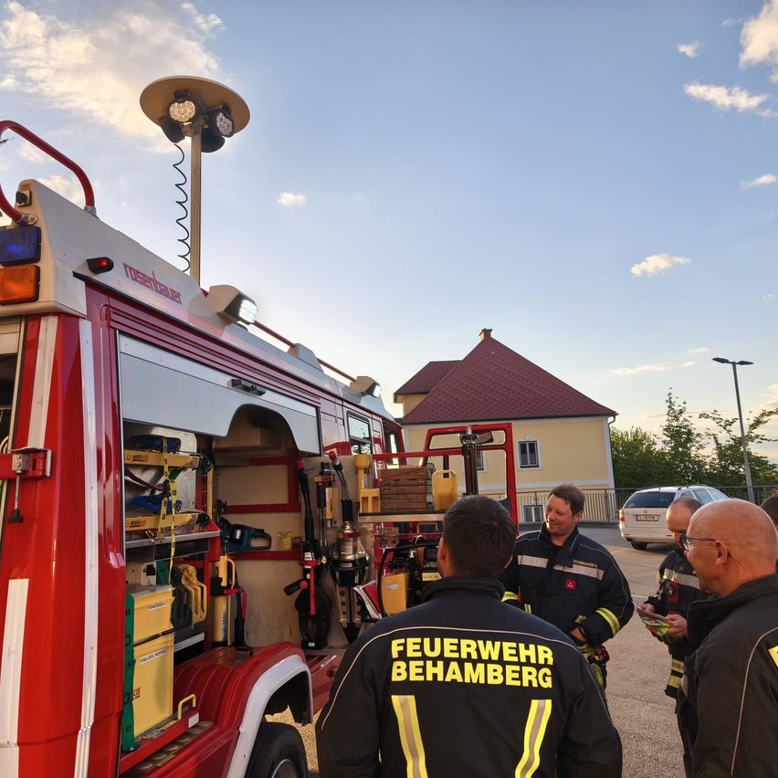 Eine Gruppe Feuerwehrleute steht um einen Feuerwehrwagen mit offenen Türen auf einem Parkplatz während des Tages.