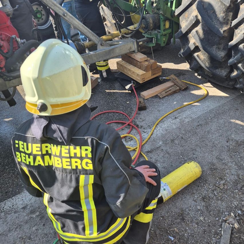 Ein Feuerwehrmann mit gelbem Helm und schwarzem Jackenmantel mit gelben Streifen sitzt auf dem Boden, möglicherweise bei einer Trainingsübung.