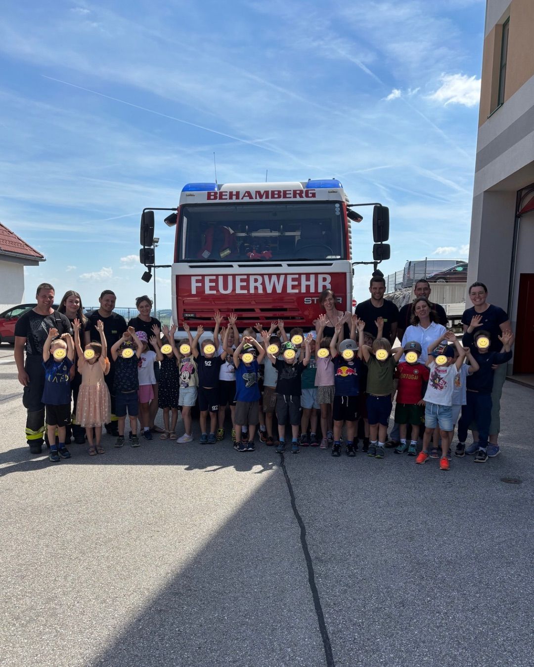 Eine Gruppe von Kindern und Erwachsenen posiert für ein Foto vor einem roten Feuerwehrauto. Sie alle lächeln und haben gelbe Kreise über ihren Augen.
