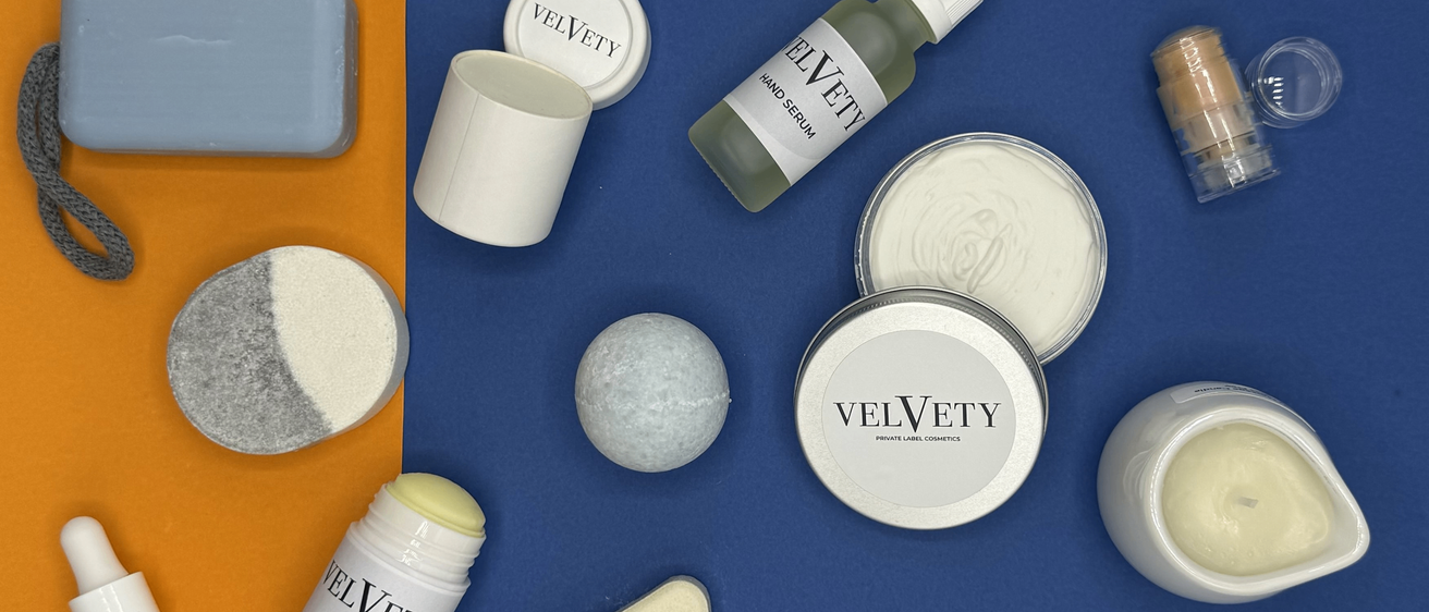 Verschiedene Kosmetikprodukte von Velvety, einschließlich einer Flasche Handserum, einem Haarpflegestift und mehreren Behältern, sind auf einer blauen Oberfläche angeordnet.