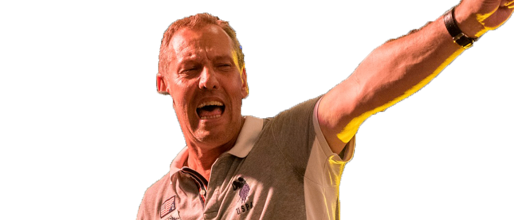 Ein Mann mit einem grauen Poloshirt und einer Uhr steht auf der Bühne, hält ein Keyboard und singt mit offenem Mund.