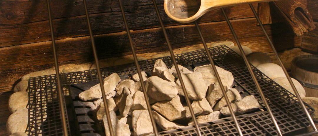 Ein hölzerner Löffel wird über einem Metallgitter gehalten, das mit Steinen gefüllt ist, möglicherweise für einen Kochprozess, vor einem hölzernen Hintergrund.