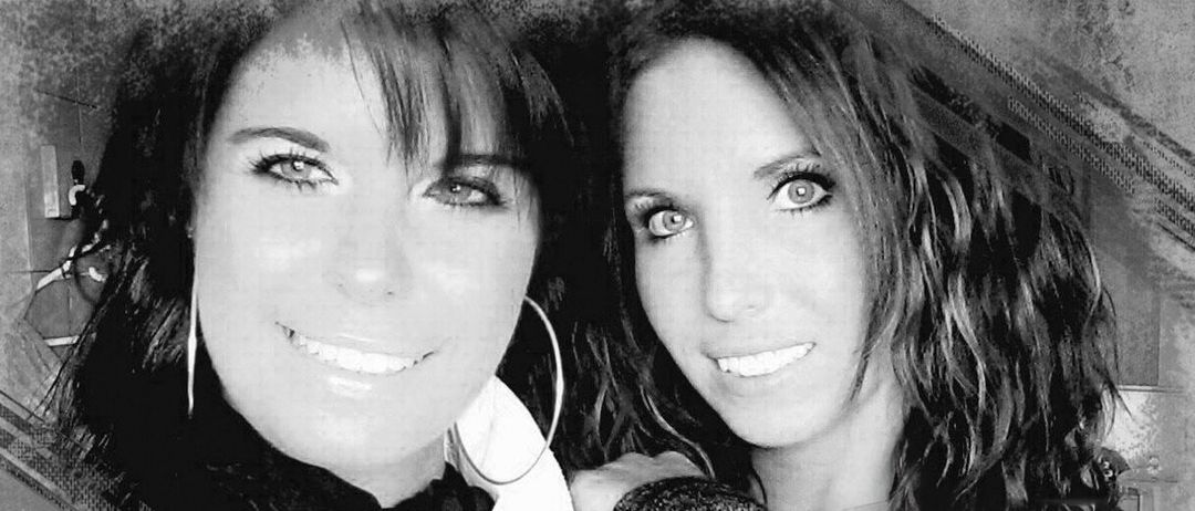 Ein Schwarz-Weiß-Foto von zwei lächelnden Frauen, von denen eine einen Schal trägt und die andere lange Haare hat.