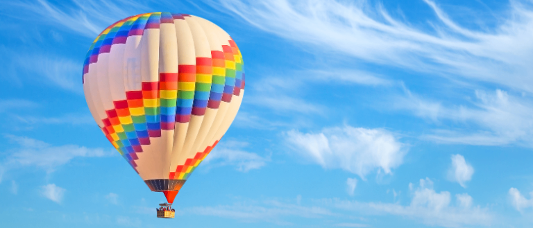 Ein farbenfroher Heißluftballon mit Regenbogenmuster schwebt im klaren blauen Himmel.