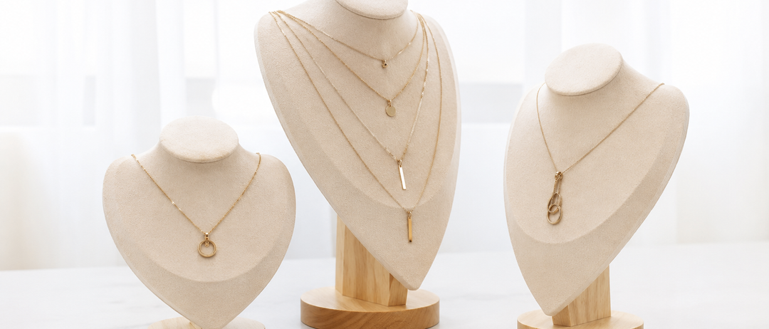 Drei Mannequins mit goldenen Halsketten zur Schau. Eines hat eine mehrreihige Kette, ein anderes einen Anhänger und das dritte eine einfache Kette.